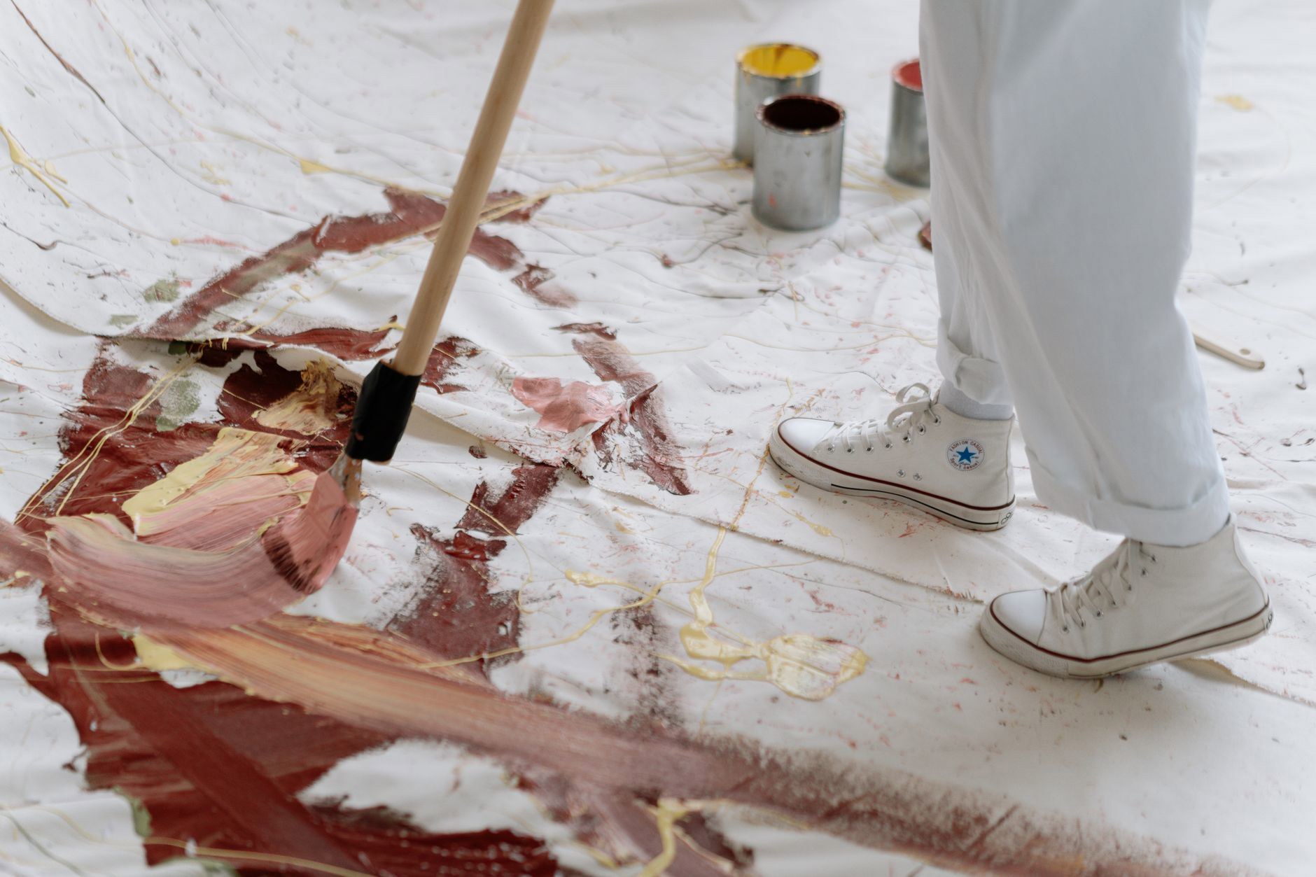 An artist uses a brush to paint abstract patterns on a large canvas placed on the floor.
