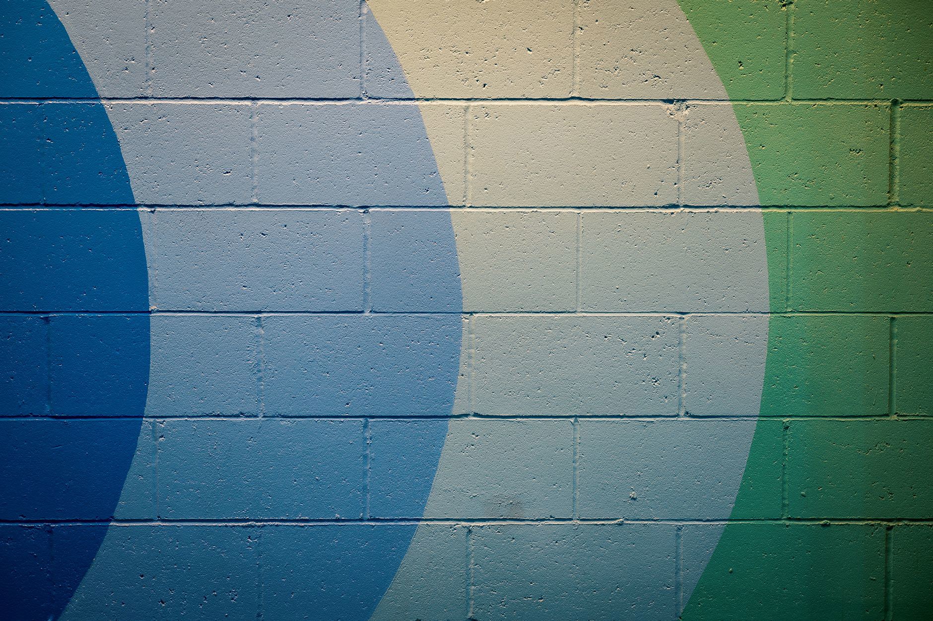 A vivid abstract mural with blue and green geometric patterns on a cement wall.